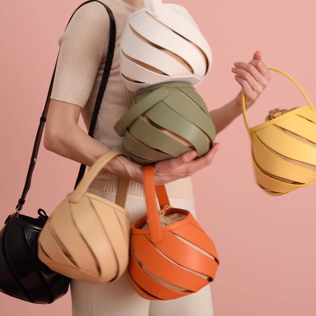 A woman holds six of the same handbag in a variety of colors. 